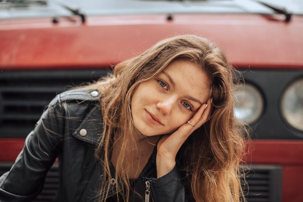 Smiling Young Woman with Tilted Head in Front of Big Red Car Hood