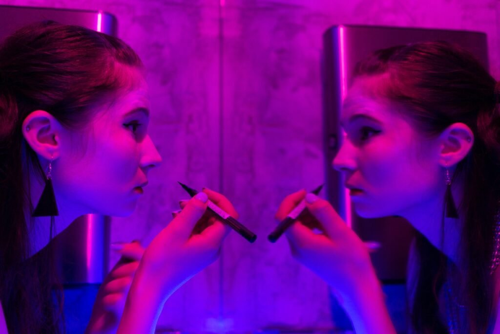 Young woman applying cosmetic in neon room