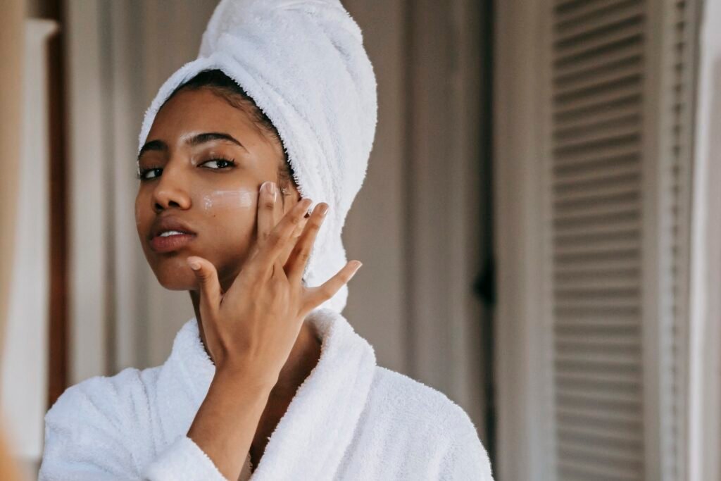 Ethnic woman applying nourishing cream on cheek against mirror