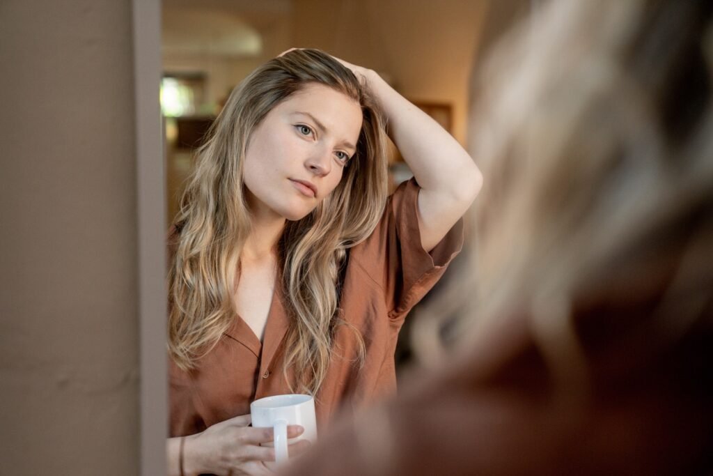 Woman Looking at Her Reflection while Holding a Ceramic Mug