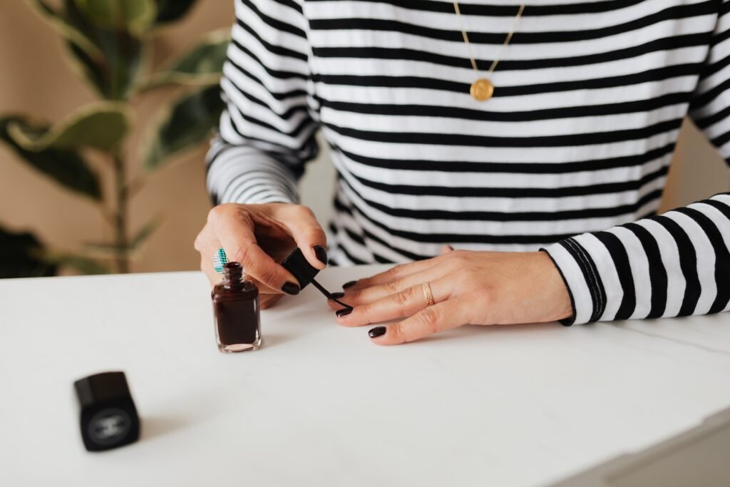 Unrecognizable female wearing casual doing manicure with nail polish while sitting at white table and spending time at weekend